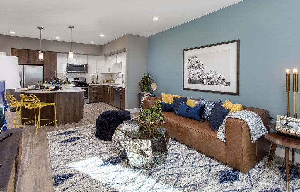 Apartments for Rent in Irvine, CA - The Royce - Open Concept Living Room with Leather-Style Couch, Blue Accent Wall, and Wood-Style Plank Flooring